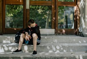 boy in black t-shirt and blue denim jeans sitting on concrete bench