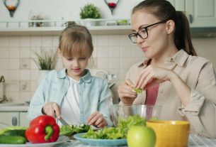 Mother and daughter preparing salad in kitchen.